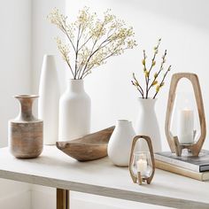 white vases and candles on a table in front of a book, candle holder and mirror