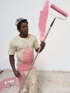 a man holding a paint roller in his hand and painting the wall with pink paint