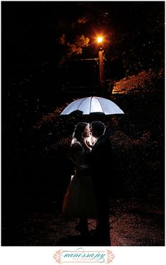 a bride and groom under an umbrella in the rain during their wedding photo session at night