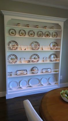 a dining room table with plates and bowls on the shelves above it, in front of a wall mounted china cabinet