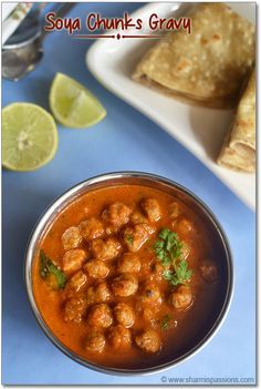 some food is in a metal bowl on a blue table with limes and pita bread