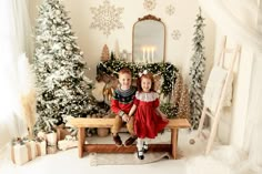 two children sitting on a bench in front of christmas trees