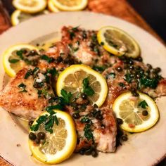 a white plate topped with fish covered in lemons and capers on top of a wooden table