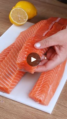 a person is cutting up salmon on a cutting board with lemons in the background