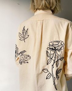 a woman with blonde hair wearing a white shirt with flowers and leaves on the back