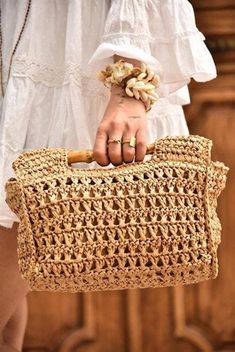 a woman is holding a crocheted bag in her hand and wearing a white dress