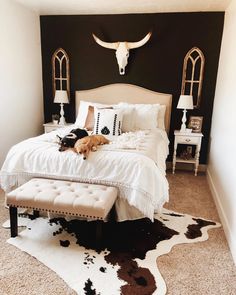 a dog laying on top of a white bed in a room with cow hide rugs