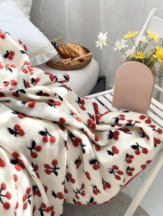 a blanket with cherries on it sitting next to a white chair and yellow flowers