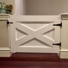 a white gate with black handles on top of a hard wood floor next to a wall