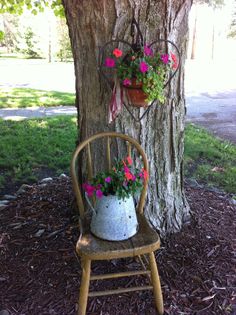 a wooden chair sitting under a tree next to a potted planter with pink flowers