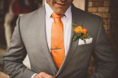 a man in a gray suit with an orange tie and flower boutonniere