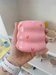 a hand holding a pink cup with hearts on it in front of other cups and bowls