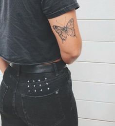 a woman with a butterfly tattoo on her left arm, wearing black jeans and a gray t - shirt