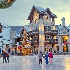 people skating on an ice rink in front of a large building with a christmas tree