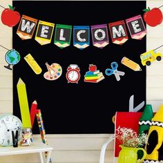 a welcome banner with school supplies hanging from it's sides in front of a blackboard