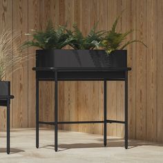 two black planters with plants in them on top of a table next to a wooden wall