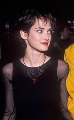 a woman with short hair wearing a black top and red lipstick in front of a crowd