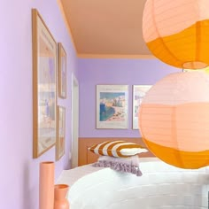 three paper lanterns hanging from the ceiling in a room with purple walls and white bedding