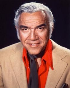 an older man with grey hair wearing a red shirt and black tie, looking at the camera