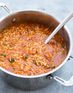 a pot filled with pasta and sauce on top of a cement floor next to a wooden spoon