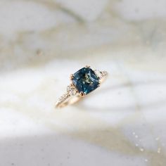 a blue diamond ring sitting on top of a marble surface