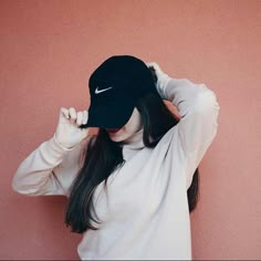 a woman wearing a black hat and white shirt is holding her hair in front of her face