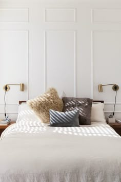 a bed with two lamps on either side and pillows on the headboard in front of it