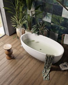 a bath tub sitting on top of a wooden floor next to potted plants in a bathroom