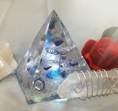 a crystal pyramid sitting on top of a table next to a red rose and other crystals