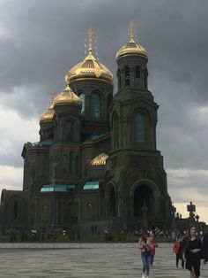 people walking in front of a large building with gold domes on it's sides