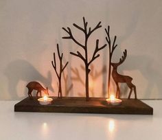 two candles are lit in the shape of deers and trees on a wooden tray