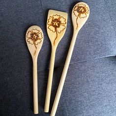 three wooden spoons with designs on them sitting next to each other in front of a blue couch