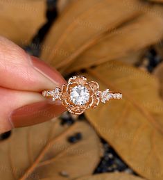 a hand holding an engagement ring in front of leaves with the top diamond setting on it