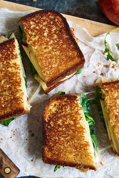 four grilled sandwiches sitting on top of a piece of paper next to an apple