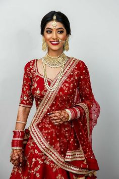 a woman in a red and gold bridal outfit with jewelry on her head, posing for the camera