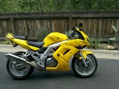 a yellow motorcycle parked in front of a wooden fence