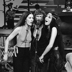 three women standing next to each other in front of a microphone and singing into a mic