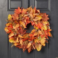 a wreath is hanging on the front door with autumn leaves and other foliage around it