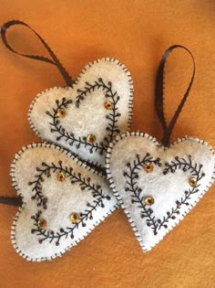 three white heart shaped ornaments hanging on a brown cloth surface with gold buttons and thread