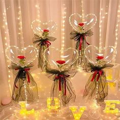 three clear vases with red roses and lights in the shape of hearts on display