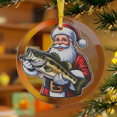 a christmas ornament hanging from a tree with a santa clause holding a fish