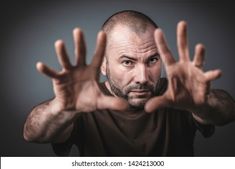 a bald man with his hands up in the air and looking at the camera, on a dark background