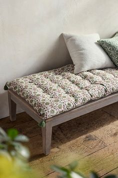 a wooden bench with pillows on it in front of a white wall and wood floor