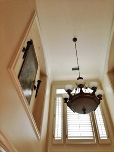 a chandelier hanging from the ceiling in a room with two windows and shutters