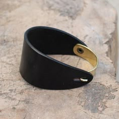 a black leather bracelet with gold plated clasps on top of a piece of wood