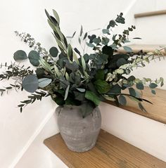 a vase filled with greenery sitting on top of a wooden stair case next to a hand rail