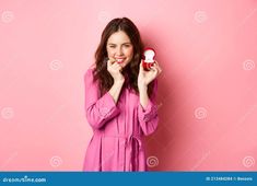 a beautiful young woman in pink dress holding an object with both hands and smiling at the camera