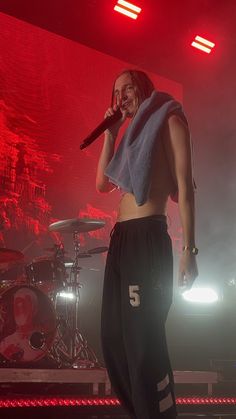 a man standing on top of a stage holding a microphone in his hand and wearing sweatpants