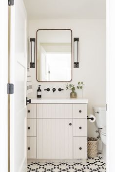 a white bathroom with black and white checkered flooring, a mirror above the sink