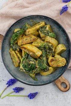 a bowl filled with pasta and spinach on top of a wooden cutting board next to purple flowers